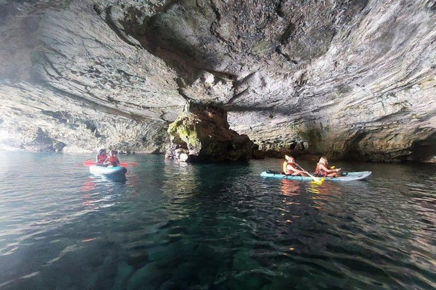 Dos personas kayakendo en una cueva con agua cristalina y paredes rocosas. 2