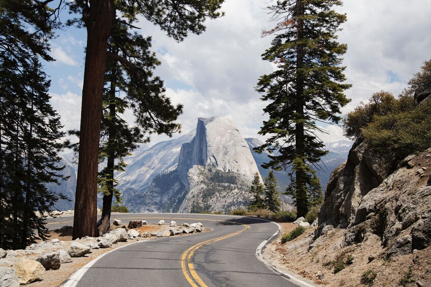 A winding mountain road flanked by tall pine trees, leading to a prominent mountain peak. 1