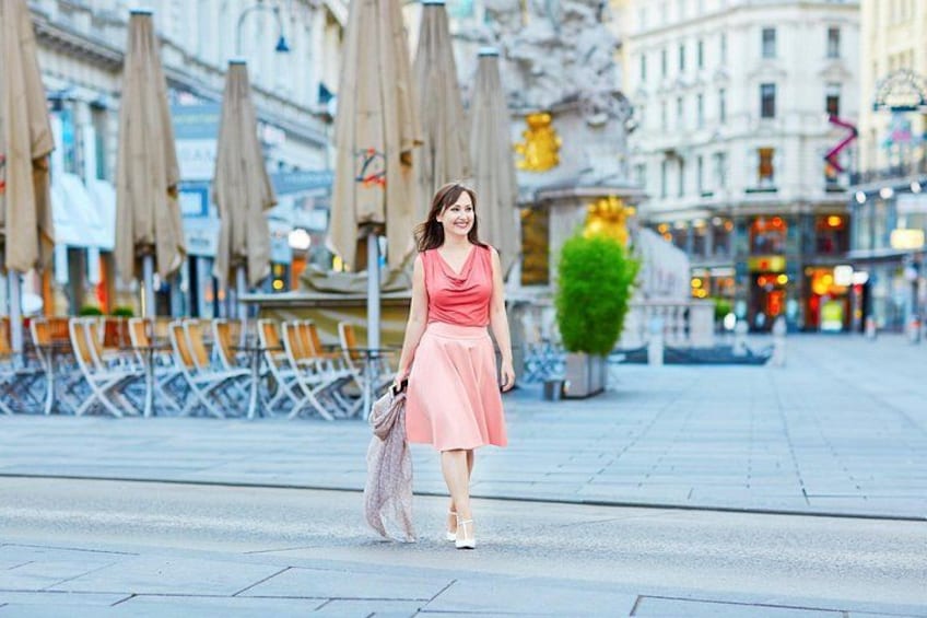 A woman in a pink dress walking on a city street with outdoor seating and buildings in the background. 1