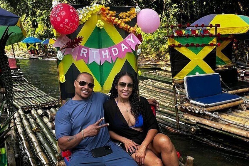A couple on a floating platform with a 'BIRTHDAY' banner, surrounded by tropical foliage and a water body. 2