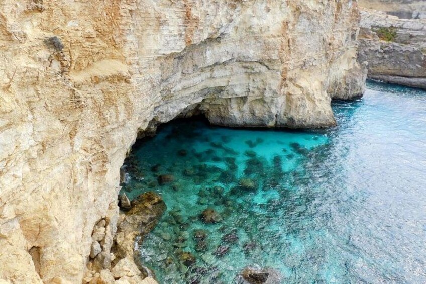 A rocky cliff with a cave entrance and clear turquoise water. 2