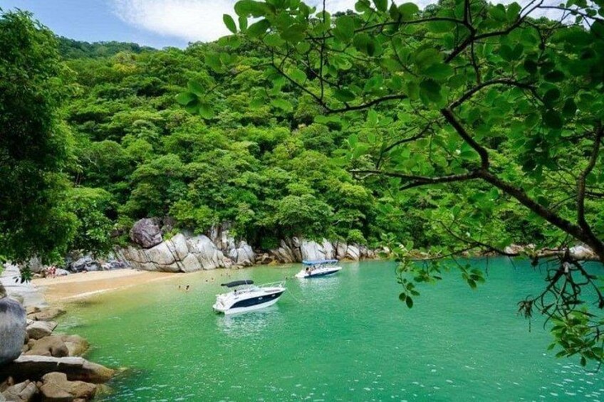 Une plage aux eaux turquoise, parsemée de bateaux, bordée d’une forêt verdoyante et ponctuée de formations rocheuses. 3