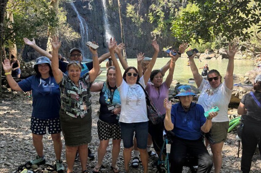 A group of people standing by a river with a waterfall in the background. 2