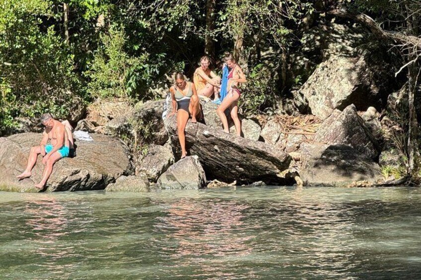 People sitting and standing on rocks by a river. 3