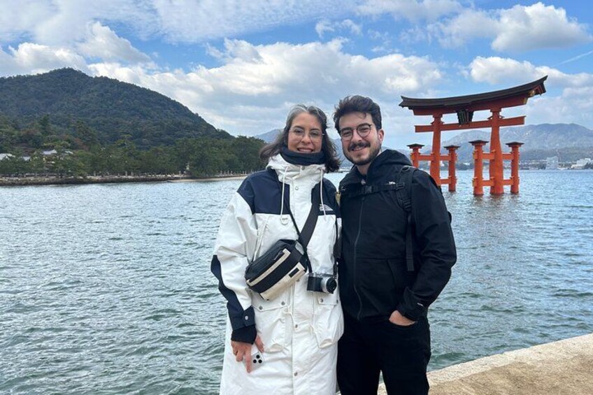Dos personas de pie junto al agua, con un torii rojo al fondo. 1