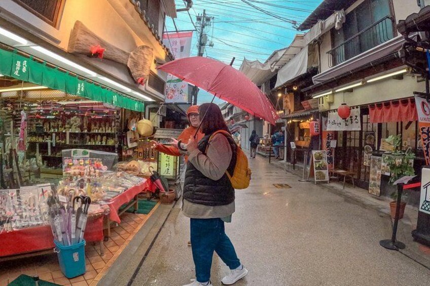Una persona cammina su una strada bagnata fiancheggiata da negozi, tenendo un ombrello. 3