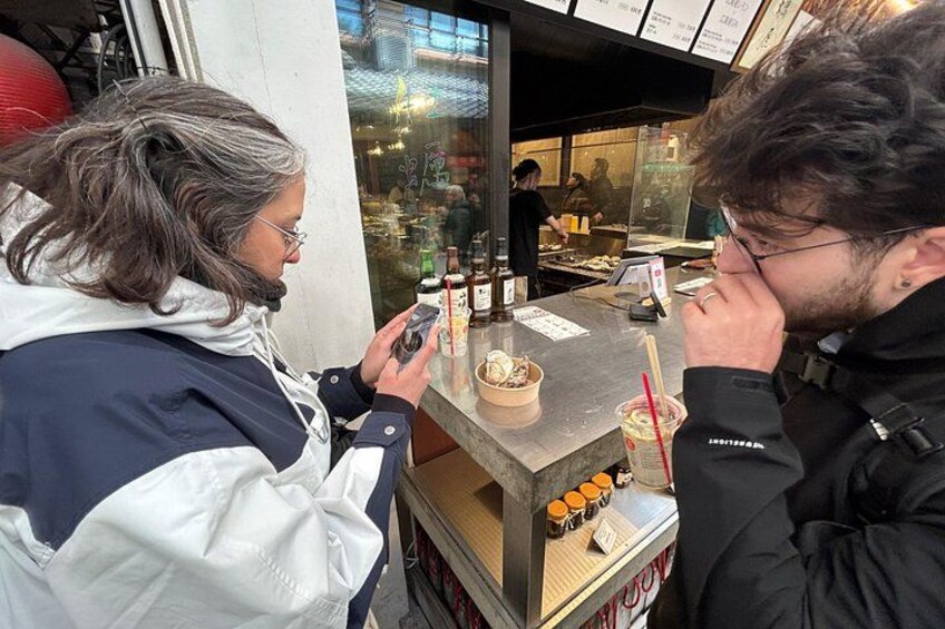 Una persona usa uno smartphone presso una bancarella di cibo, con una ciotola di cibo e condimenti sul bancone. 4