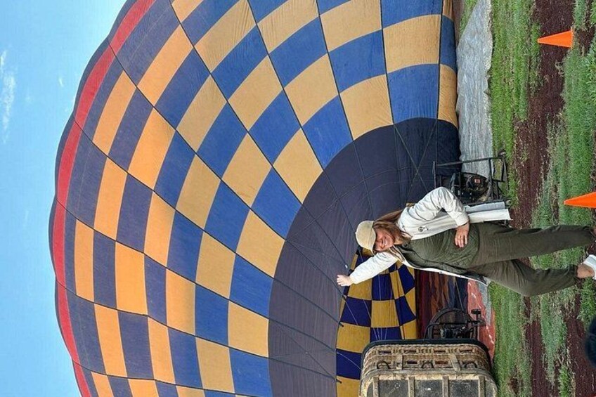 Een persoon staat onder een grote, kleurrijke luchtballon, met een grasveld op de achtergrond. 2