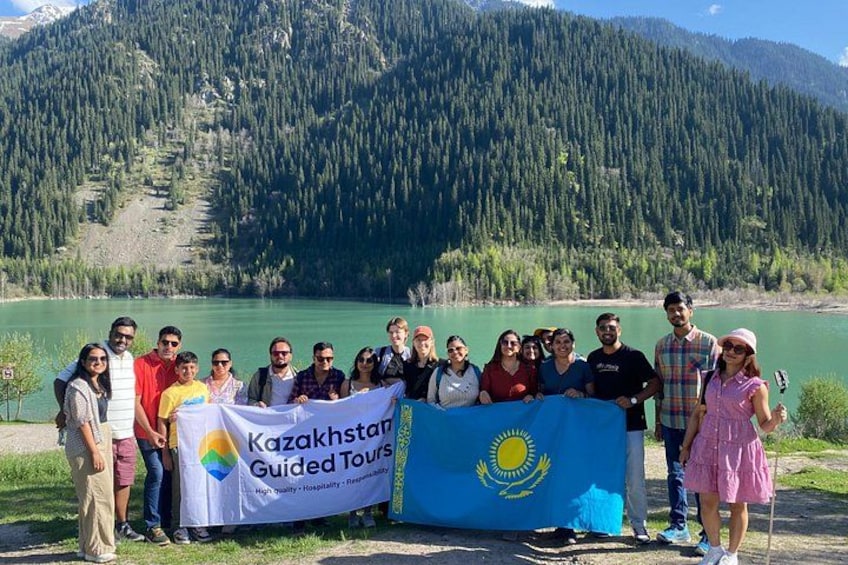 A group of people standing by a lake with a banner reading 'Kazakhstan Guided Tours.' 1