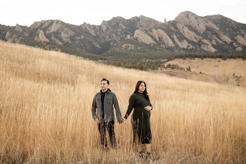 A couple holding hands in a field with mountains in the background. 2