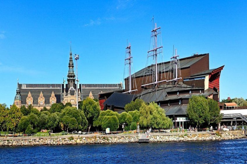 A historic building with a tall tower, a modern structure with a sloped roof, and a body of water in the foreground. 4