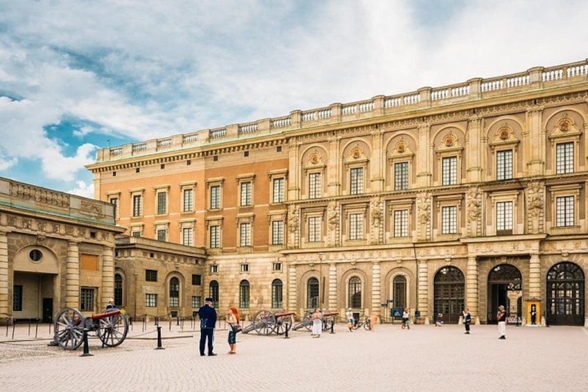 A historic building with classical architecture, a paved courtyard, and horse-drawn carriages. 1