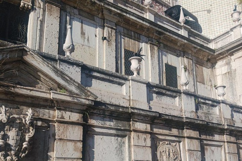 Facciata di un edificio dall'aspetto antico, con dettagli architettonici classici, tra cui modanature elaborate e uno stemma decorativo. 3
