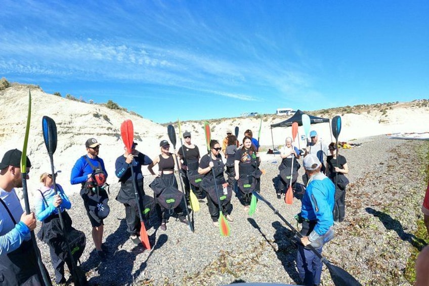 A group of people holding paddles, standing on a rocky beach with a tent in the background. 1