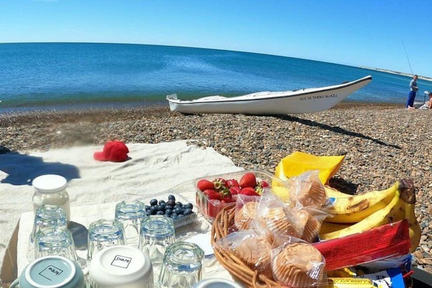 A picnic setup on a pebbled beach with a boat in the background. 3