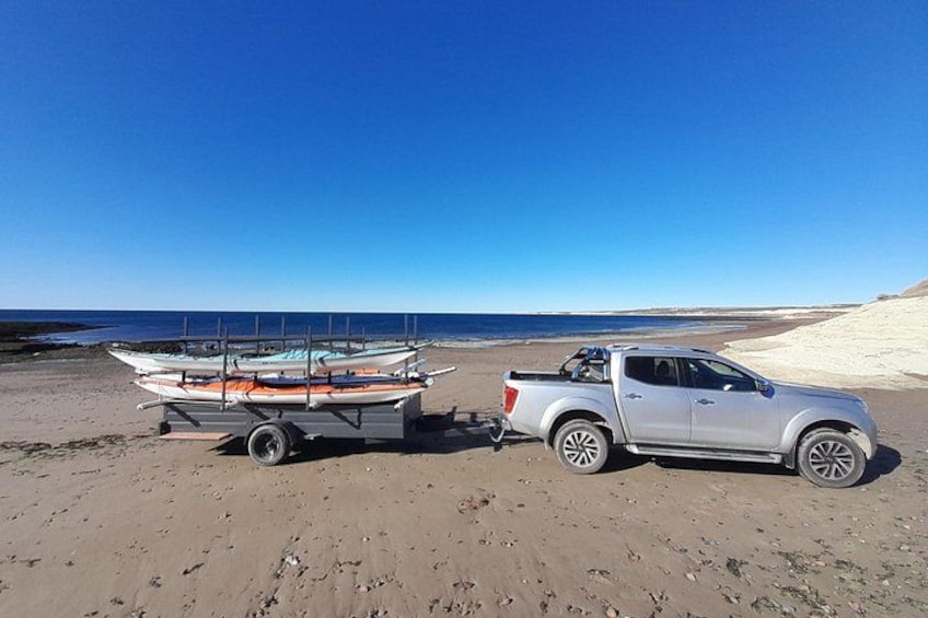 A beach with a white pickup truck towing a trailer with boats. 2