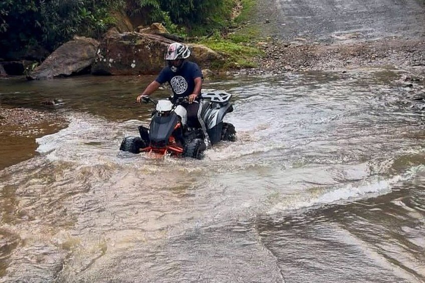 A person riding a quad bike through a shallow river. 2