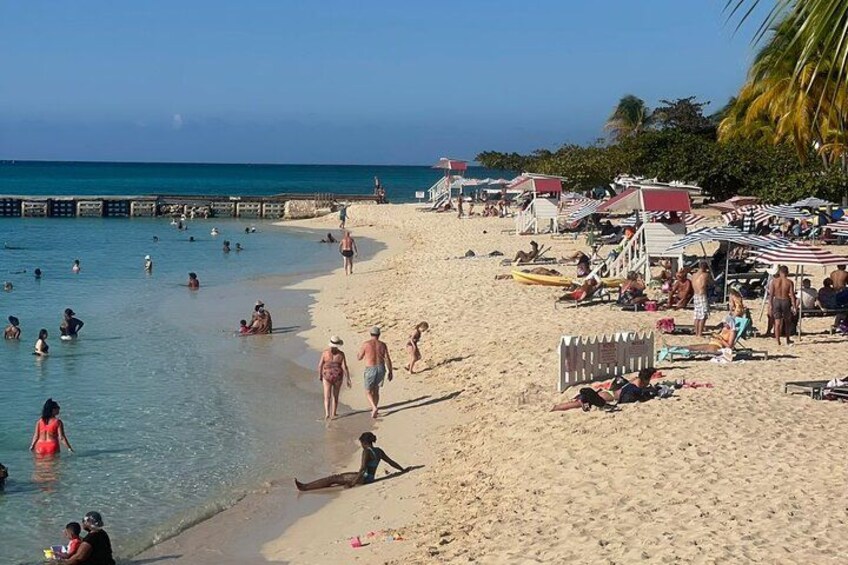 Een strand met mensen die zwemmen, zonnebaden en wandelen. Er staan strandparasols en ligbedden. 3