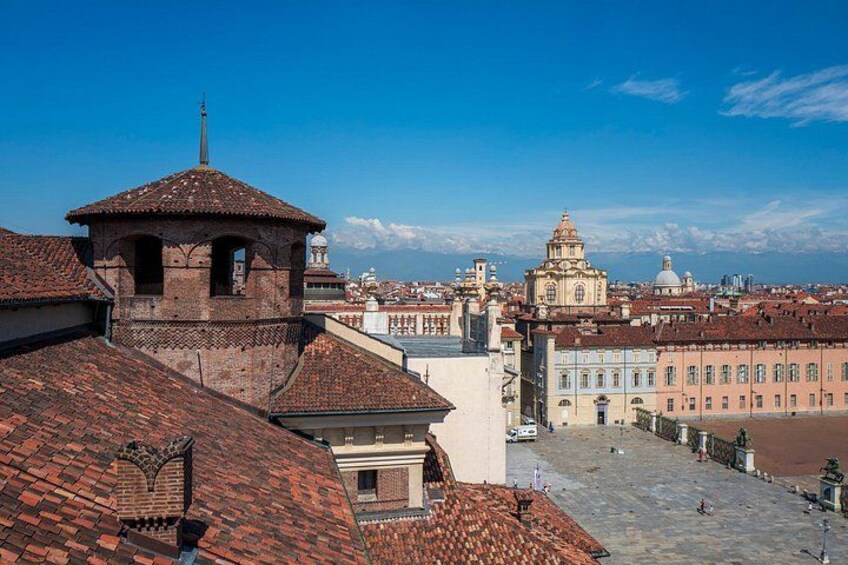 Paesaggio urbano con un edificio a cupola in lontananza, una torre con tetto a punta e una piazza lastricata in primo piano. 1