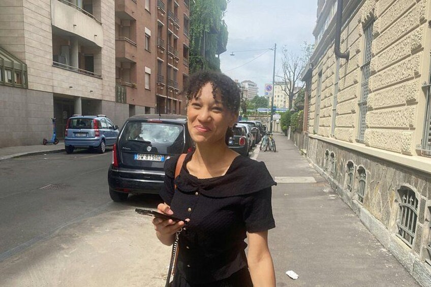 Una persona in piedi su un marciapiede, con edifici e auto parcheggiate sullo sfondo. 5
