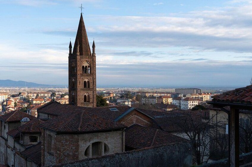 Una chiesa con un campanile slanciato, uno skyline urbano con edifici e una catena montuosa in lontananza. 4