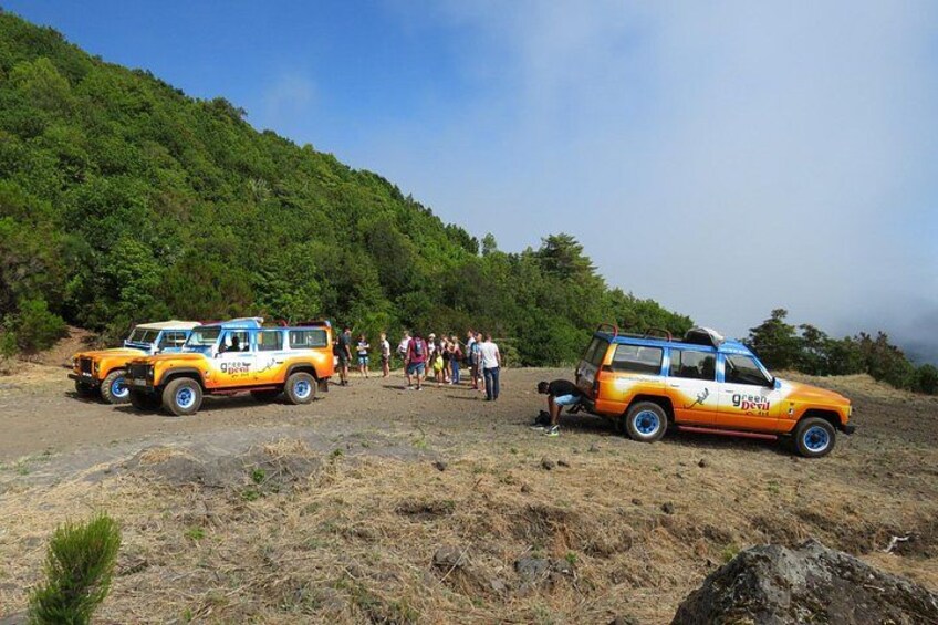 Two orange vehicles parked on a hillside with a group of people standing nearby. 5