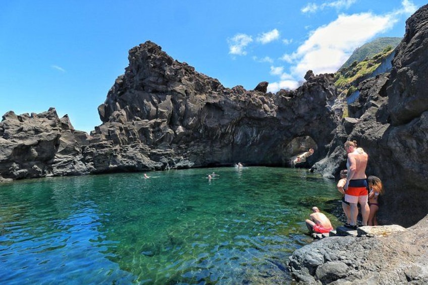 A rocky coastal area with clear water, people swimming, and a person standing on a rock. 1