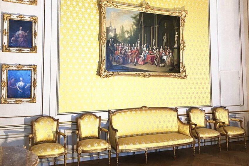 A room with a large ornate painting, a sofa, and several chairs. 3