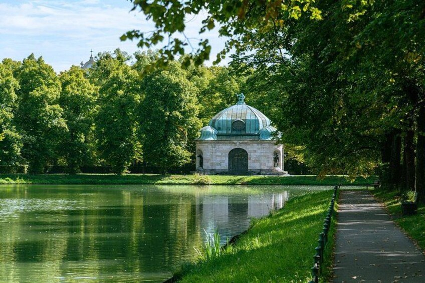 A tranquil park with a pond, a pathway, and a small building with a dome. 4