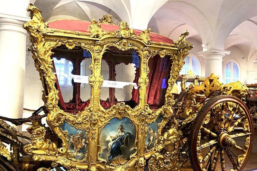 An ornate carriage with gold detailing and red velvet curtains, displayed indoors with arched ceilings. 5