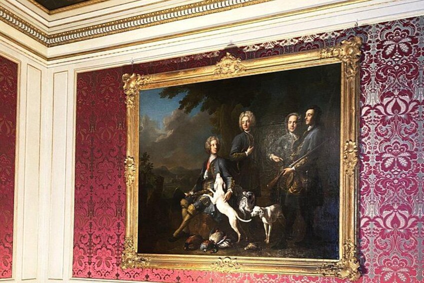 A classical painting with ornate gold framing, set against a red patterned wall. 3