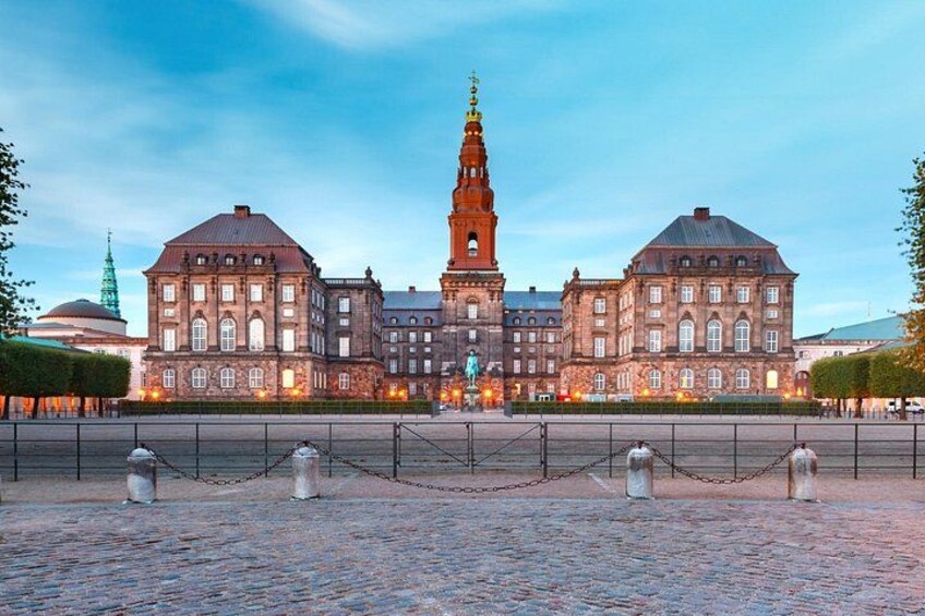 A historic building with a prominent tower, surrounded by a paved area with a chain barrier. 1