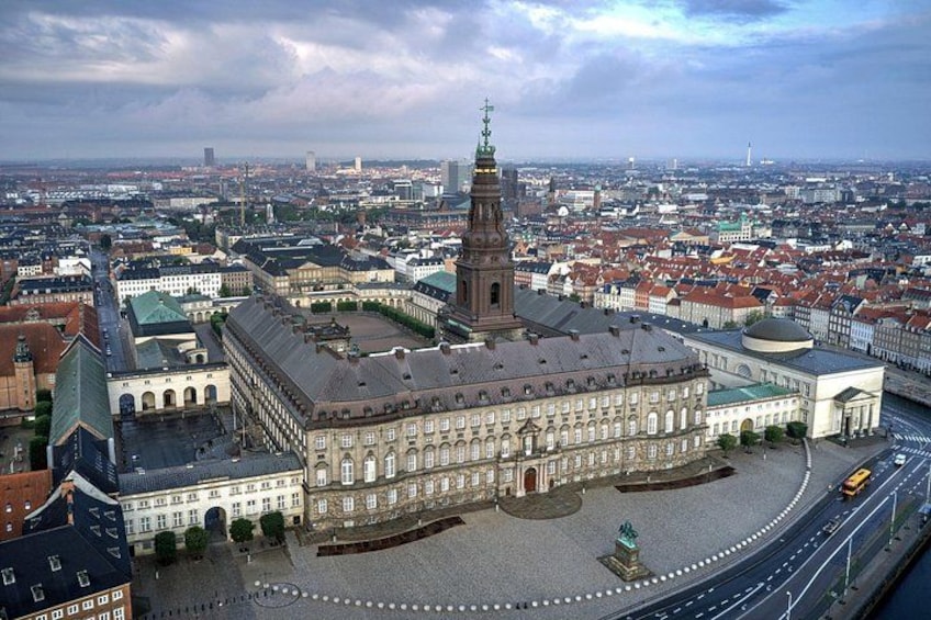 A historic building with a prominent tower, surrounded by a cityscape with various other buildings and a wide road. 3