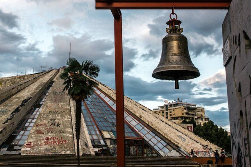 A bell tower with a staircase leading up to it, a palm tree, and a building in the background. 3