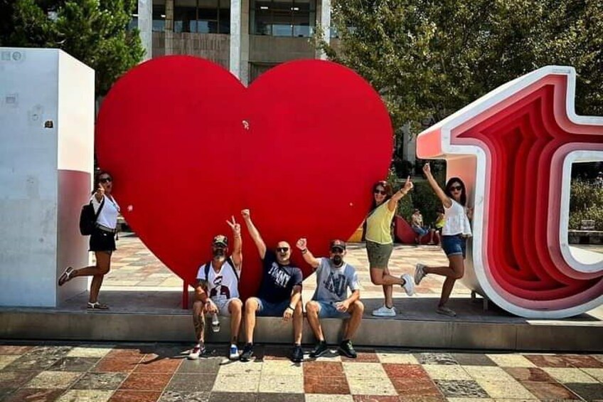 A group of people posing in front of a large red heart-shaped sculpture and a red number '1' sign. 1