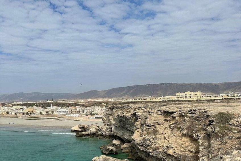 Un paysage côtier caractérisé par une rive rocheuse, une plage de sable et un ensemble de bâtiments situés au loin. 5