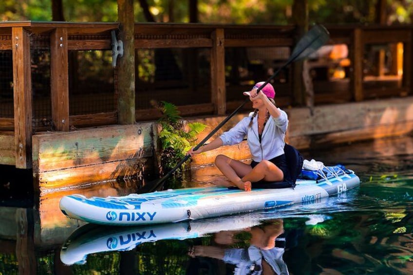 A person sitting on a paddleboard near a wooden dock. 2
