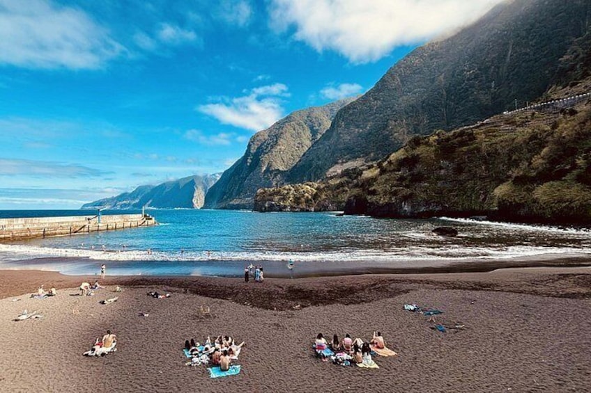 A beach with people sunbathing, a rocky coastline, and a clear sky. 5
