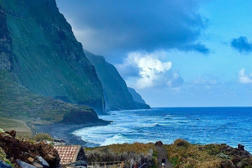A coastal landscape with steep cliffs, a rocky shoreline, and a clear blue sky. 4