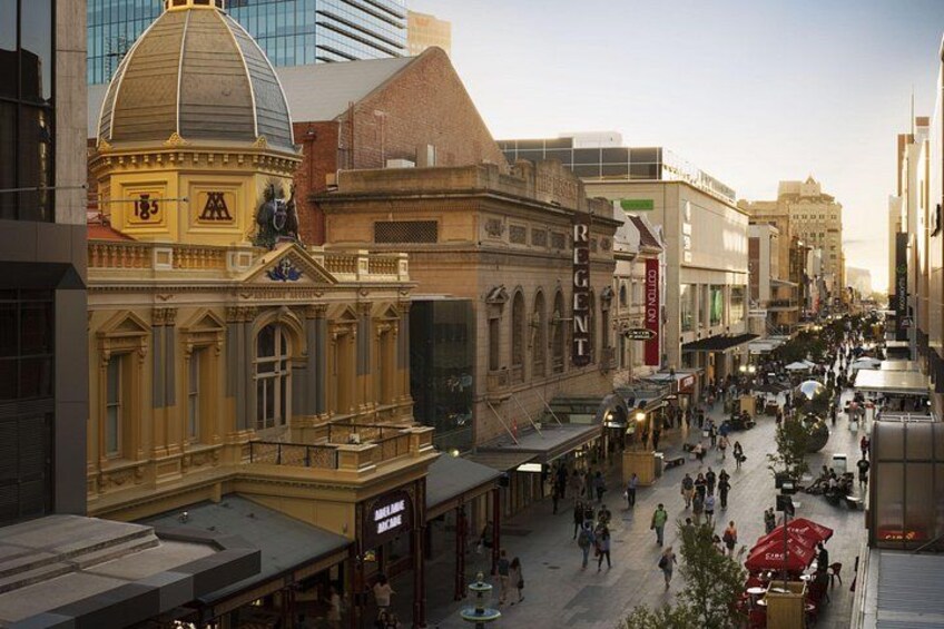 A bustling urban street with historic architecture, including a prominent building with a dome and columns, and a variety of shops and cafes. 2