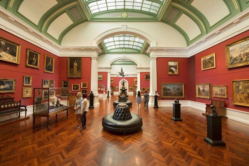 An art gallery with wooden floors, red walls, and a central fountain. 1