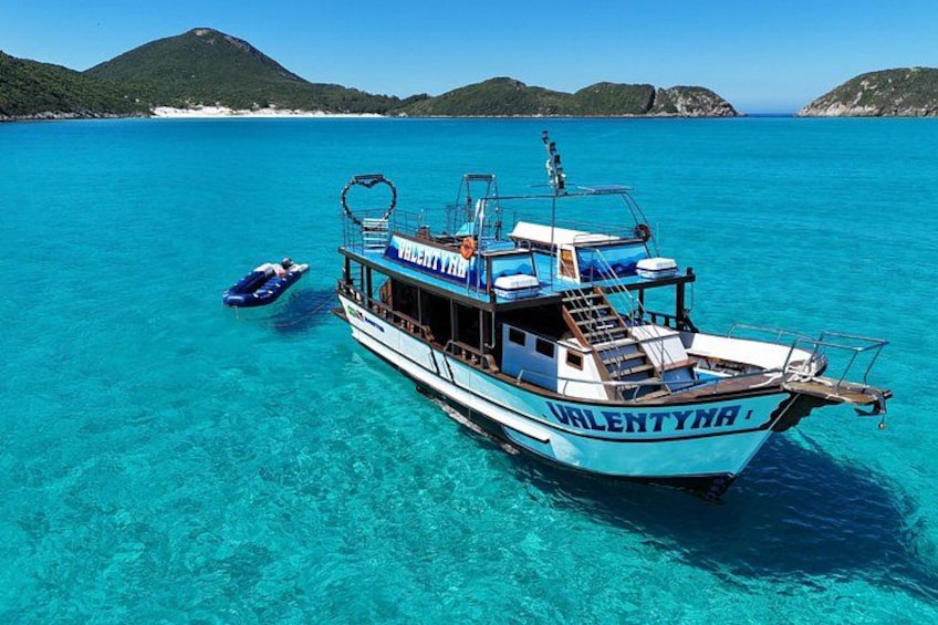 Een boot genaamd 'Valentyna' op helder turquoise water, met een bergachtig landschap op de achtergrond. 1