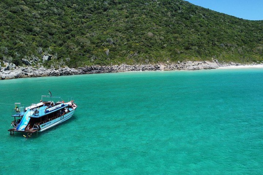 Een boot op turquoise water, met een bebost heuvel op de achtergrond. 3