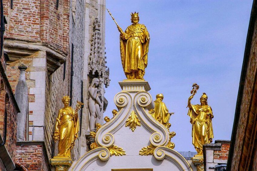 Una estatua dorada en la cima de una estructura blanca ornamentada con diseños intrincados, sobre un fondo de un edificio de ladrillo. 2