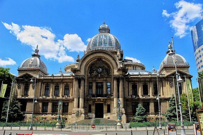 Un edificio grande y ornamentado con una cúpula central y dos cúpulas más pequeñas, rodeado de un jardín cuidado y un cielo azul despejado. 4
