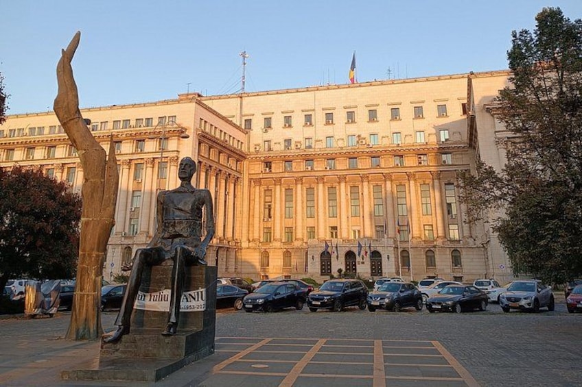 Una estatua de una figura sentada frente a un edificio grande con varias banderas. 3