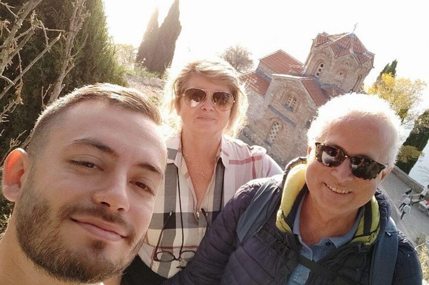 Three people standing in front of a historic building with a red roof and a bell tower. 3