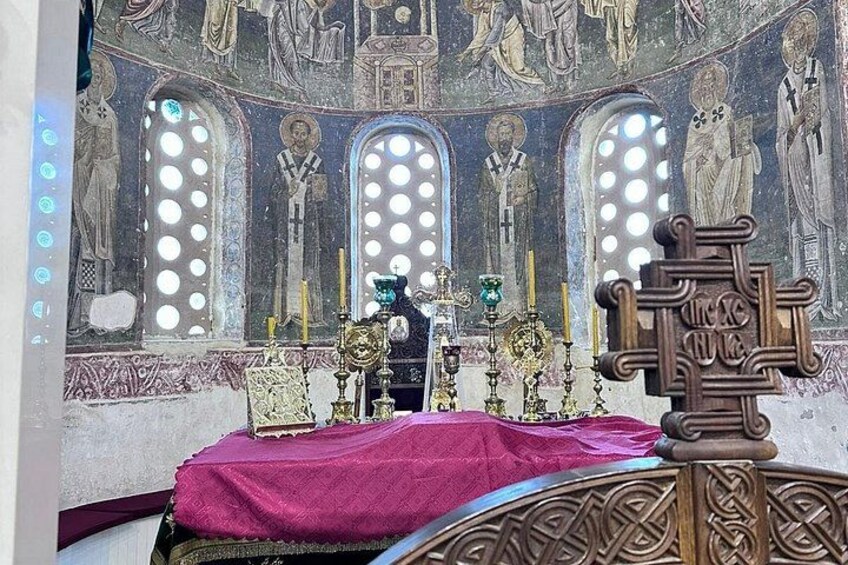 A church interior with a red cloth-covered altar, ornate wooden furniture, and a detailed mosaic wall. 4