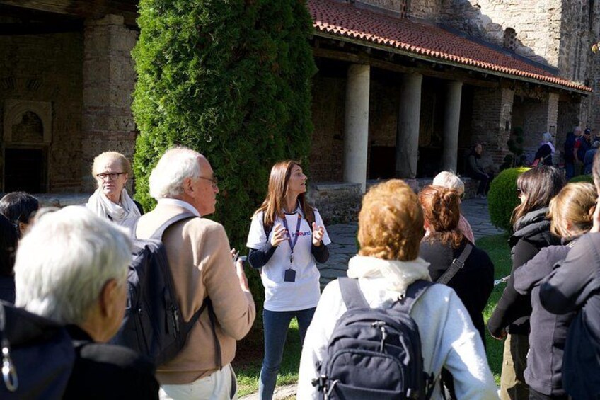 A group of people standing outdoors, some with backpacks, in front of a building with columns and a tiled roof. 5