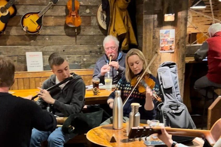 En grupp människor som spelar stränginstrument i en rustik miljö med träväggar och träbänkar. 2